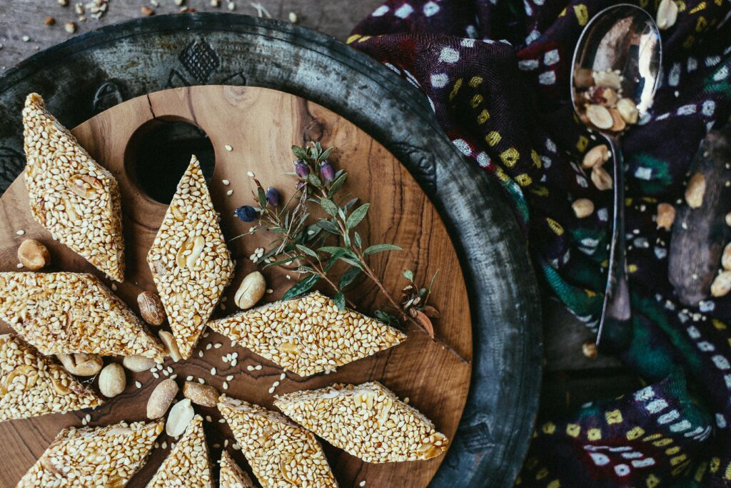 Close-up of sesame and peanut brittle on a wooden serving tray, with rustic decor.